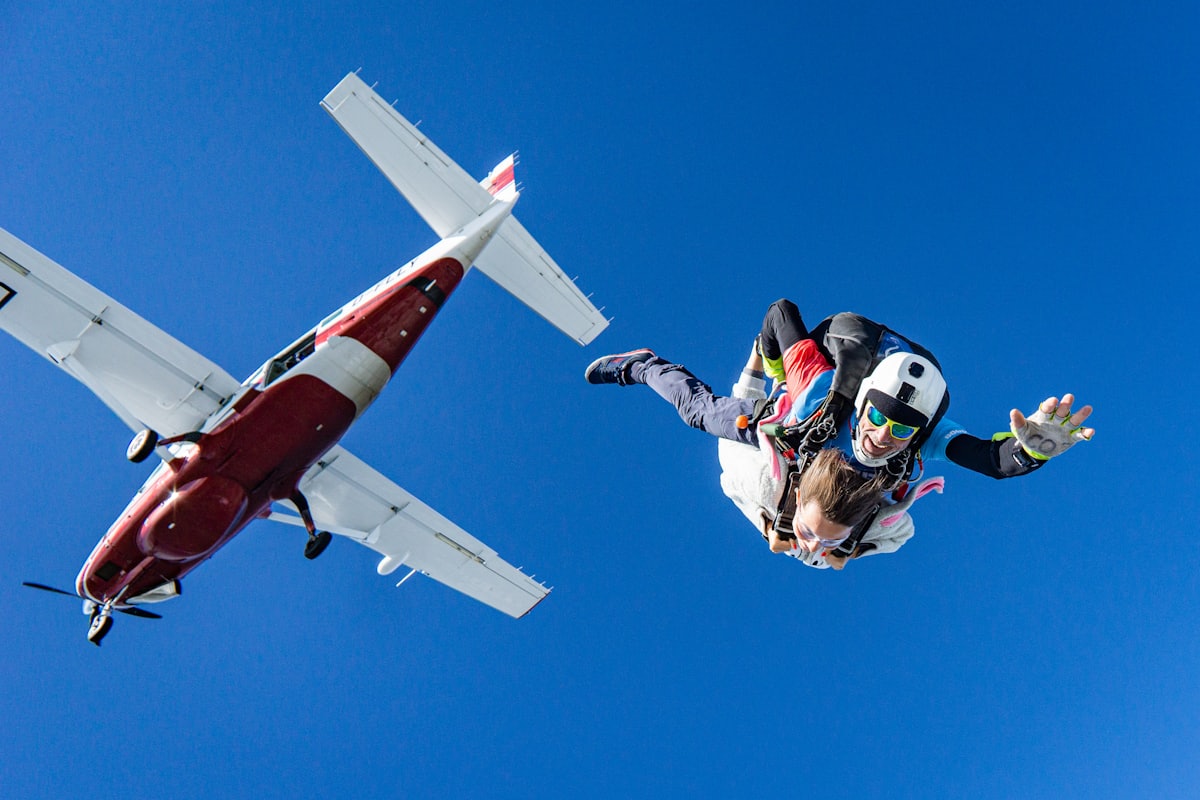 A tandem skydiver leaving a small plane against a deep blue sky.